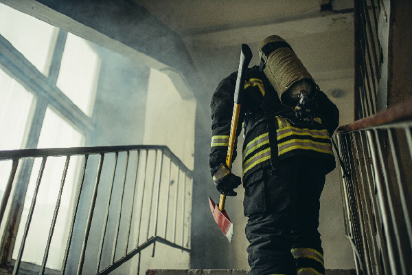 Firefighter with axe and breathing apparatus climbing a smoke-filled building stairwell.