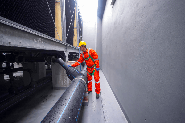 Utility worker in safety gear inspecting industrial piping beside building equipment