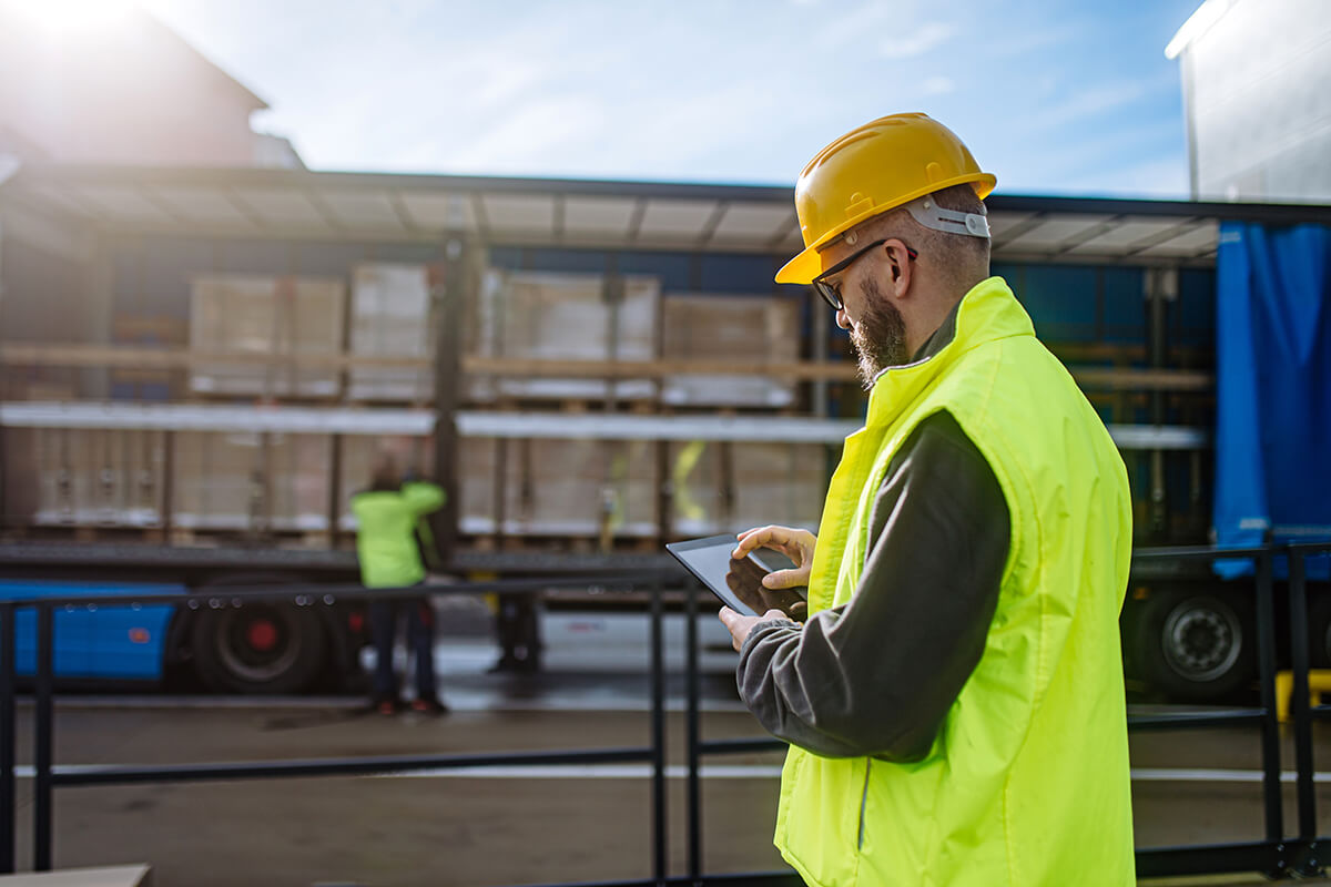 Field technician using a tablet beside a commercial transport truck to manage fleet operations and remote communications.